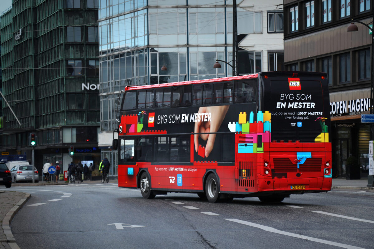 Dobbeltdækkerbus med LEGO-reklame kører gennem byens gader, fremviser potentialet i busreklame